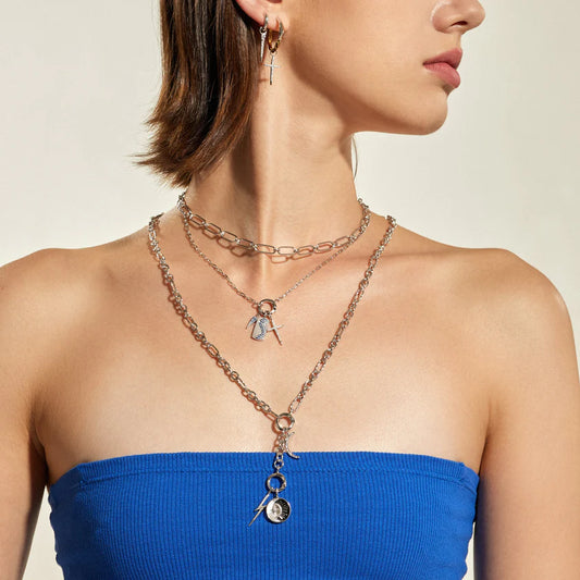 Woman wearing a layered necklace with blue top on a neutral background