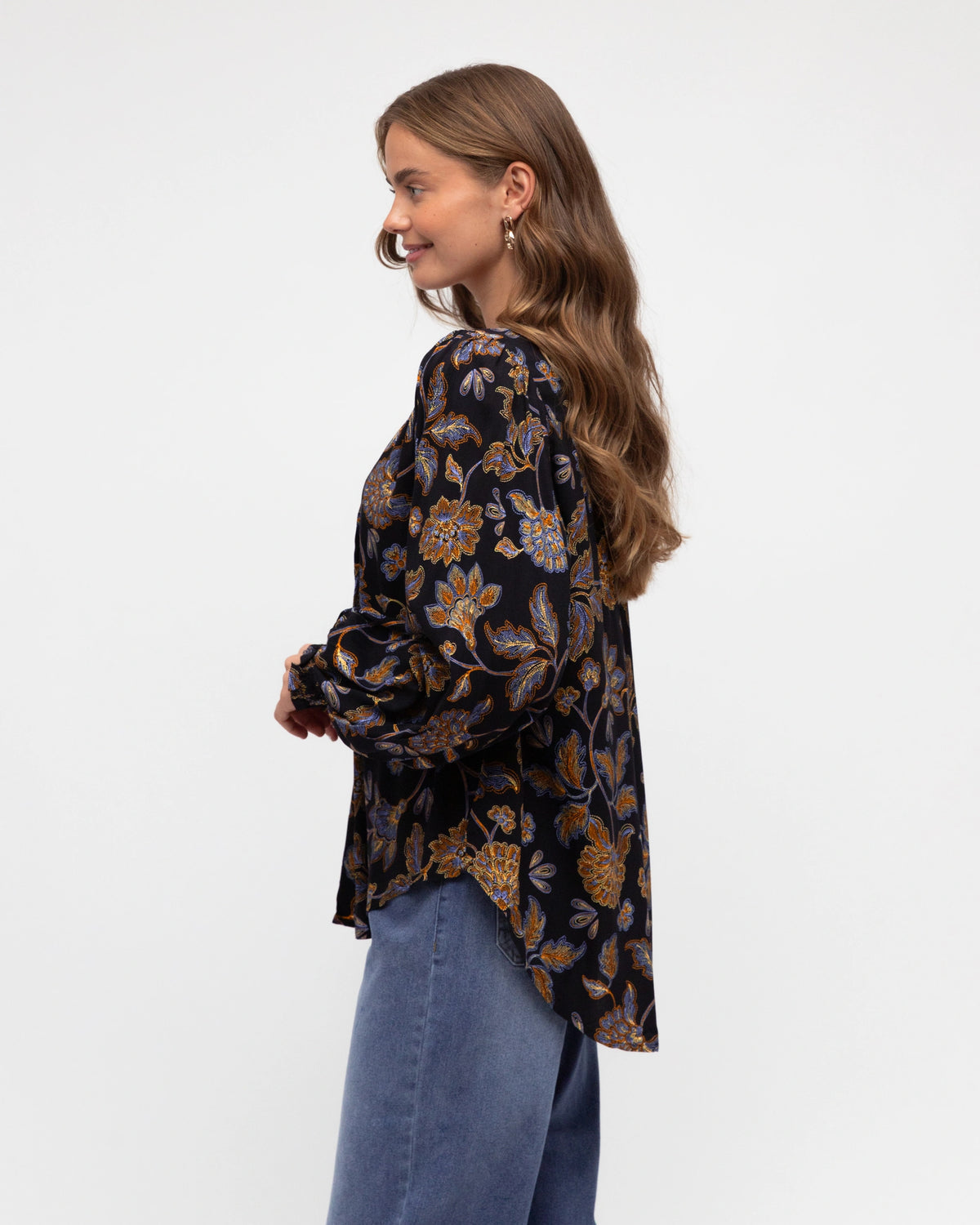 Woman wearing a patterned blouse and jeans on a white background